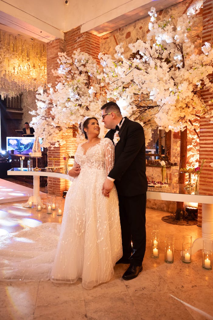 A joyful couple at their indoor wedding surrounded by decorative cherry blossoms and warm lighting.