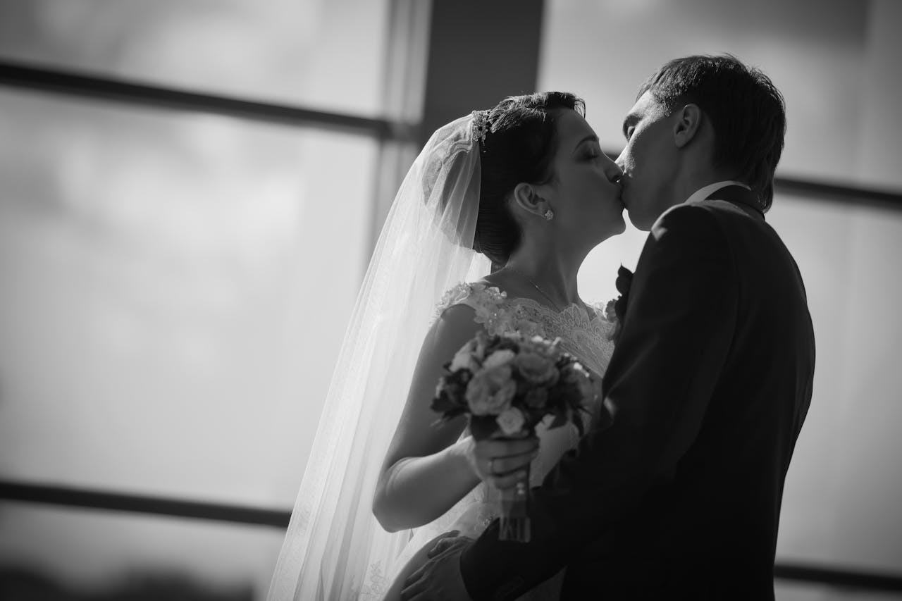 A romantic black and white photo capturing a bride and groom sharing a kiss on their wedding day.