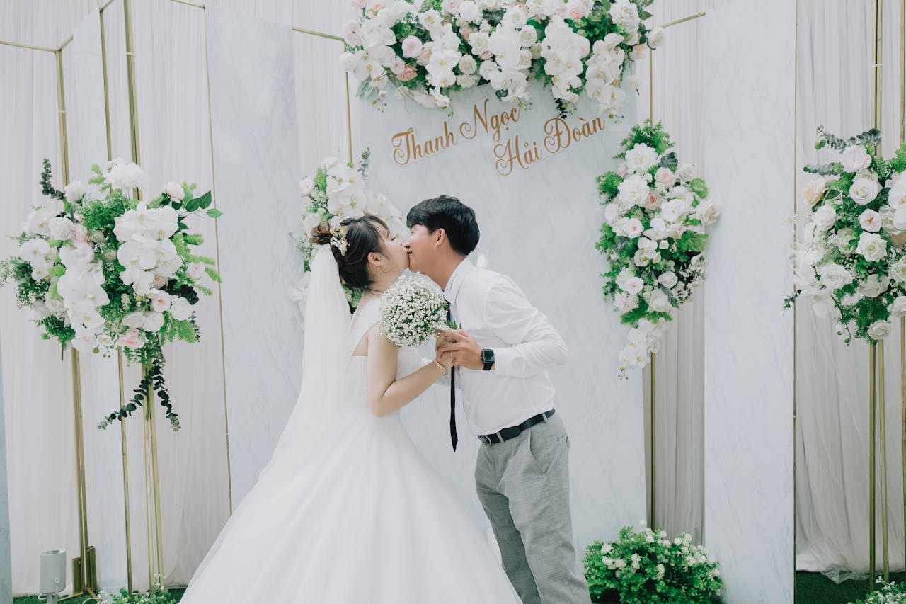 Bride and groom share a romantic kiss under a flower arch at their indoor wedding ceremony.